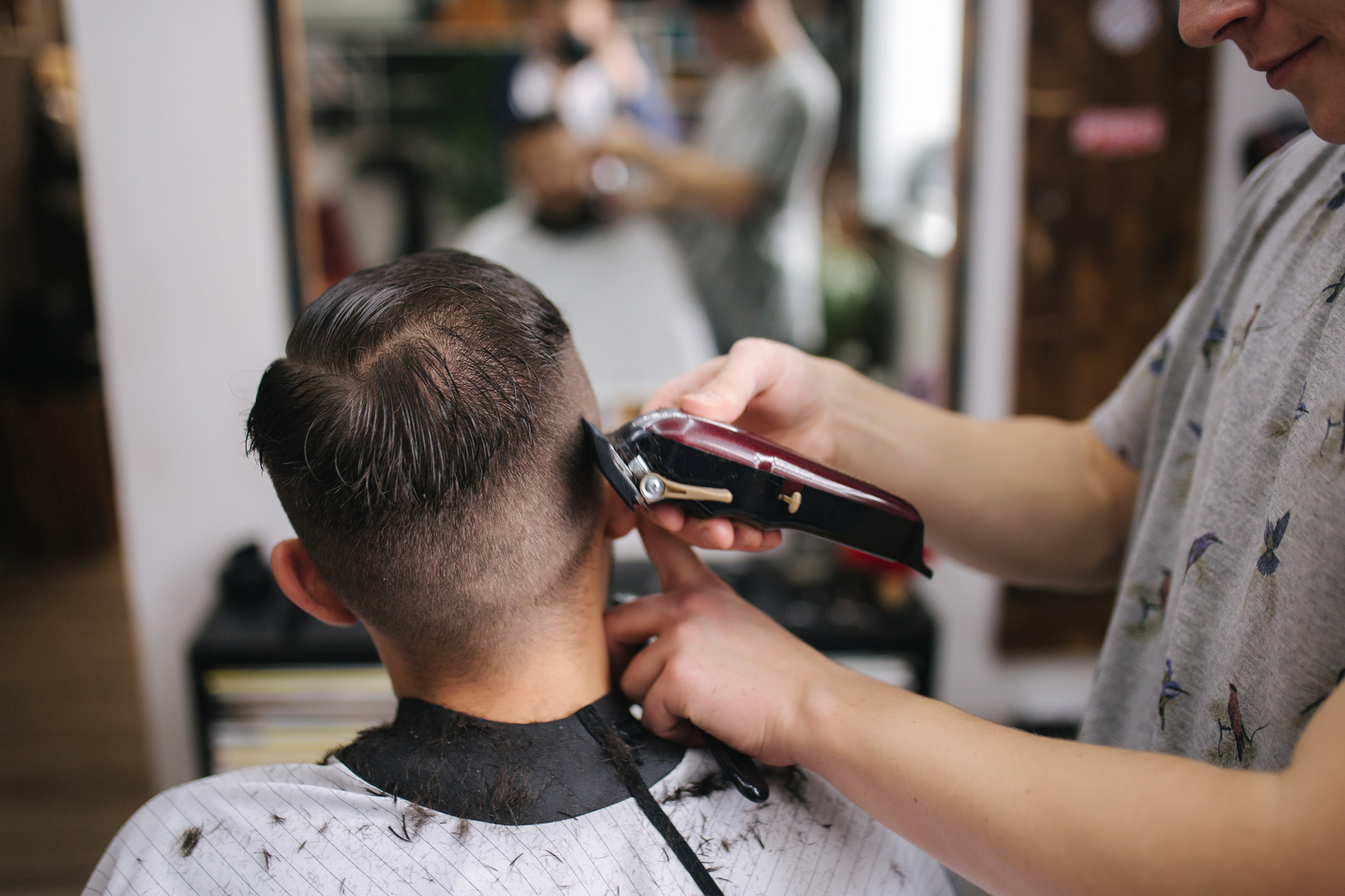Back view of Men in beauty salon. Men's haircut in a barbershop. New haircut style 2021. Professional hairdresser uses a hair clipper for fringing hair